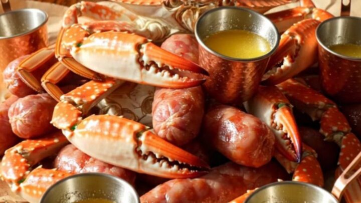 A close-up of a steaming Crockpot filled with blue crab claws, smoked sausage, and corn in a spiced Old Bay broth.
