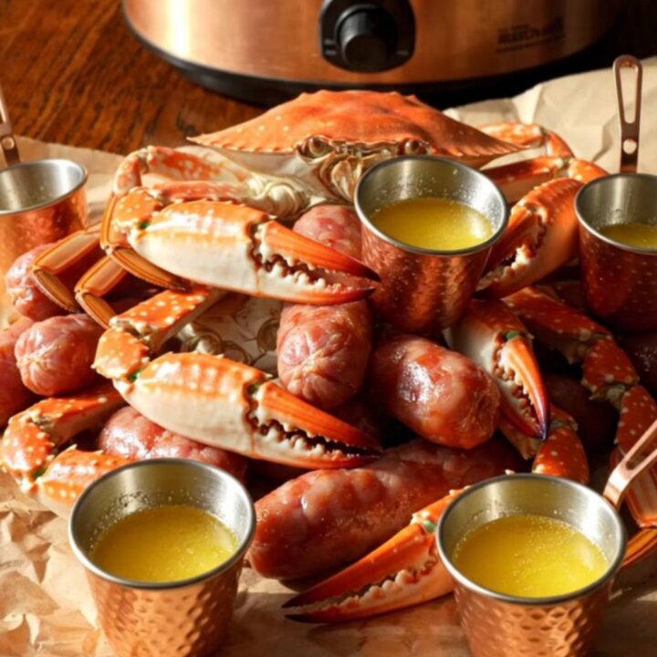 A close-up of a steaming Crockpot filled with blue crab claws, smoked sausage, and corn in a spiced Old Bay broth.