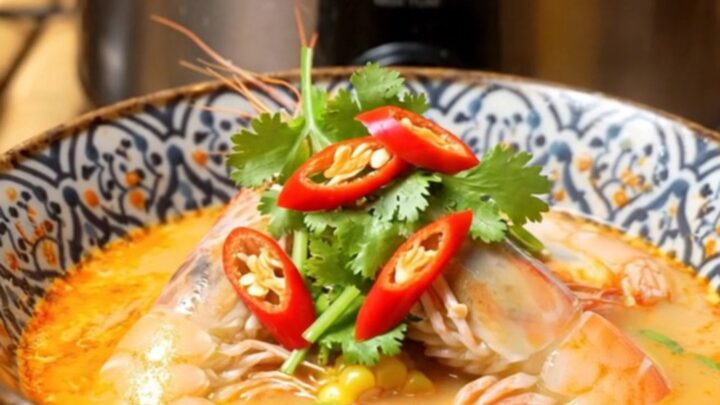 A close-up of a slow cooker filled with a vibrant red Thai Tom Yum seafood boil featuring prawns and mussels.