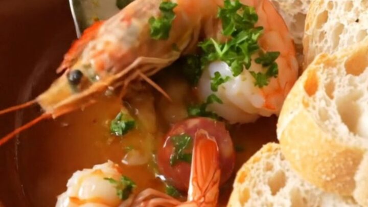 A rustic clay dish filled with sizzling Spanish garlic shrimp and chorizo in golden oil.