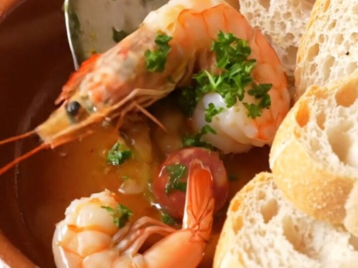 A rustic clay dish filled with sizzling Spanish garlic shrimp and chorizo in golden oil.