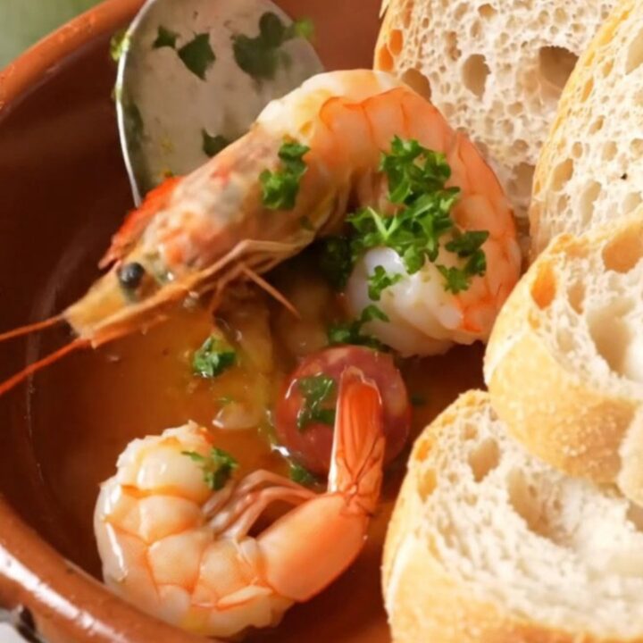 A rustic clay dish filled with sizzling Spanish garlic shrimp and chorizo in golden oil.