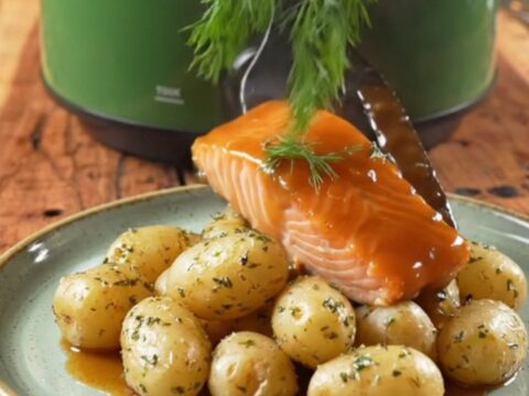 A close-up of bourbon-glazed sockeye salmon and tender baby potatoes in a green ceramic slow cooker.