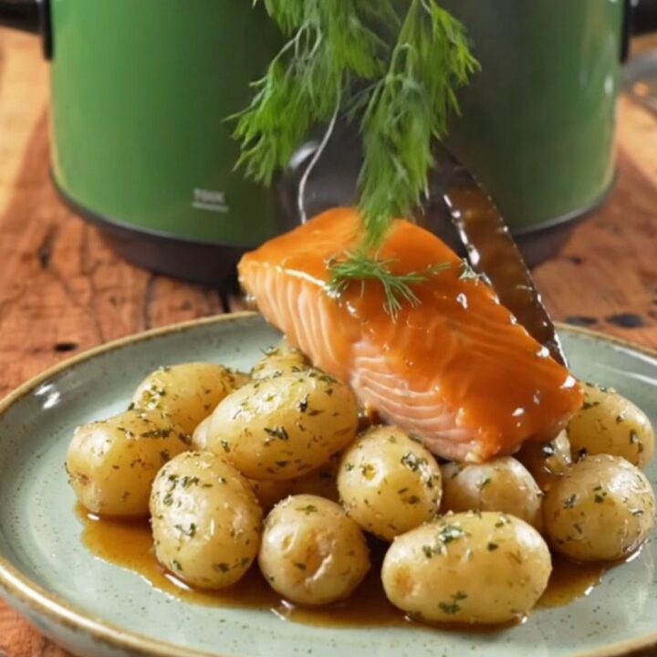 A close-up of bourbon-glazed sockeye salmon and tender baby potatoes in a green ceramic slow cooker.