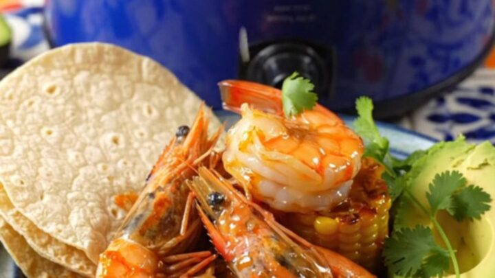 A close-up shot of fiery Camarones a la Diabla in a blue Crockpot, featuring large shrimp and charred corn.