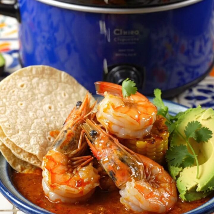 A close-up shot of fiery Camarones a la Diabla in a blue Crockpot, featuring large shrimp and charred corn.