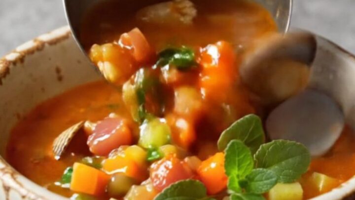 A steaming bowl of Manhattan clam chowder with whole clams and smoky bacon in a cozy kitchen.
