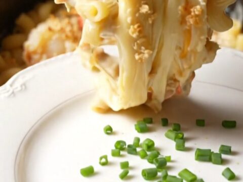 A close-up of a champagne-gold ceramic slow cooker filled with creamy lobster mac and cheese topped with golden brioche
