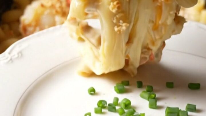 A close-up of a champagne-gold ceramic slow cooker filled with creamy lobster mac and cheese topped with golden brioche
