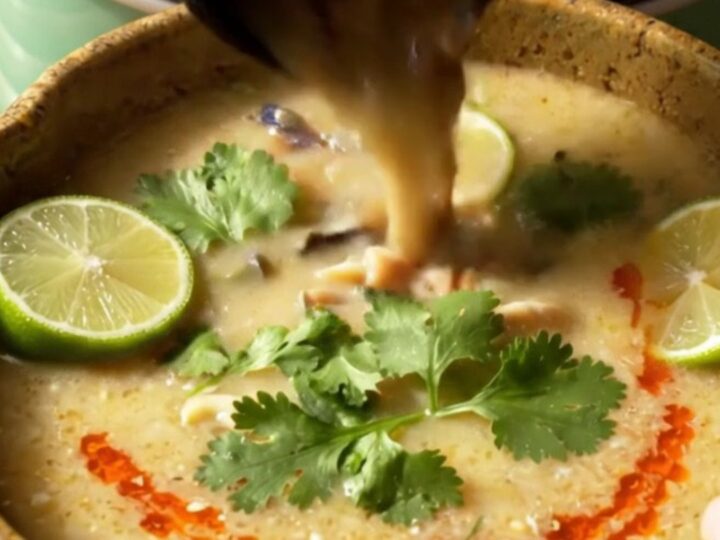 A ceramic bowl filled with creamy coconut lime chowder, featuring chunks of halibut and open Manila clams