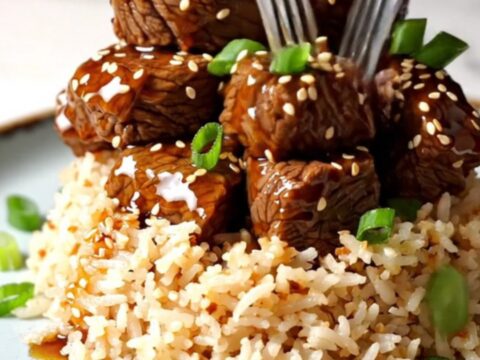 A close-up of tender beef short rib bites glazed in a sticky, amber-colored honey sesame sauce in a ceramic Crockpot.