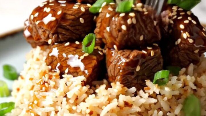 A close-up of tender beef short rib bites glazed in a sticky, amber-colored honey sesame sauce in a ceramic Crockpot.