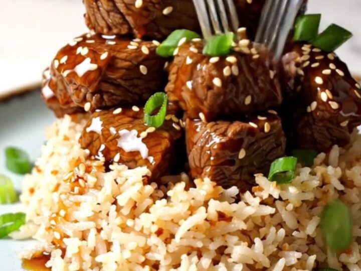 A close-up of tender beef short rib bites glazed in a sticky, amber-colored honey sesame sauce in a ceramic Crockpot.