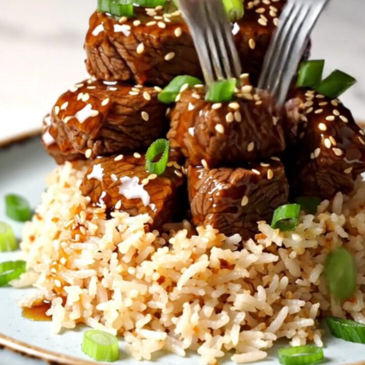 A close-up of tender beef short rib bites glazed in a sticky, amber-colored honey sesame sauce in a ceramic Crockpot.