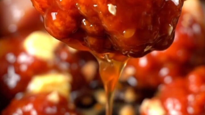 A close-up of glossy Korean chicken bites in a ceramic slow cooker, topped with crushed peanuts and green onions.