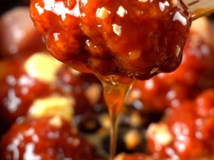 A close-up of glossy Korean chicken bites in a ceramic slow cooker, topped with crushed peanuts and green onions.