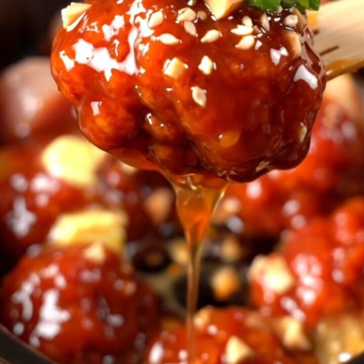 A close-up of glossy Korean chicken bites in a ceramic slow cooker, topped with crushed peanuts and green onions.