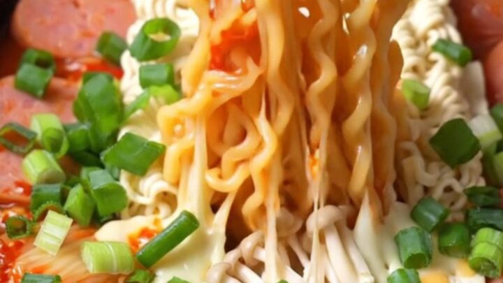 A close-up of a slow cooker filled with vibrant Korean Army Stew featuring ramen, kimchi, Spam, and melted cheese.