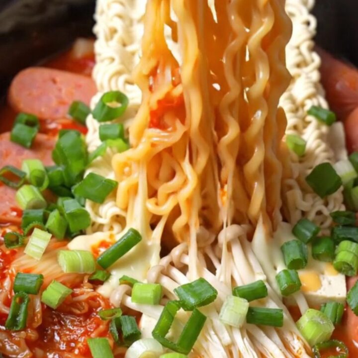 A close-up of a slow cooker filled with vibrant Korean Army Stew featuring ramen, kimchi, Spam, and melted cheese.