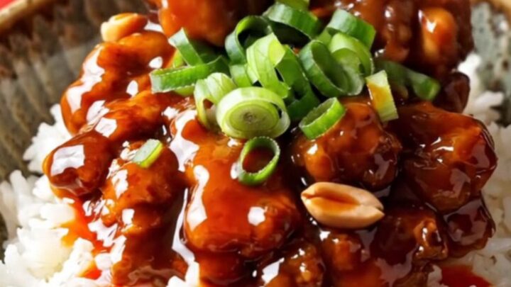 A vibrant bowl of Kung Pao chicken served over white rice with visible peanuts and scallions.