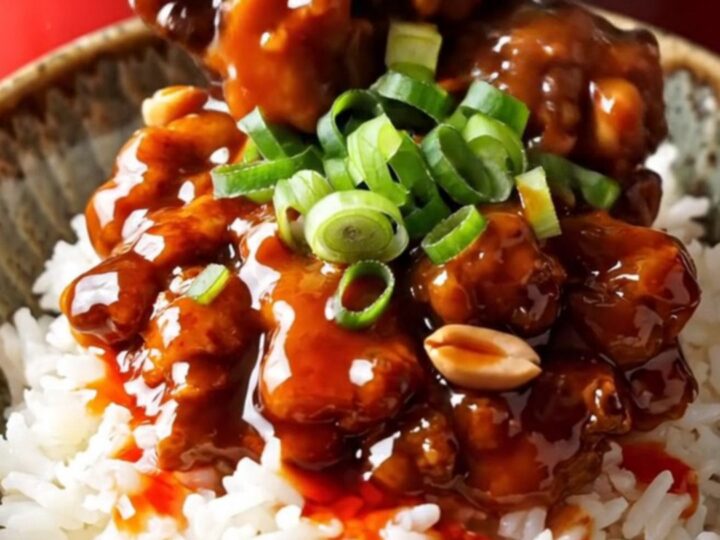 A vibrant bowl of Kung Pao chicken served over white rice with visible peanuts and scallions.