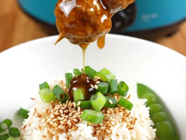 A close-up view of sticky teriyaki chicken meatballs glistening with glaze in a ceramic slow cooker.