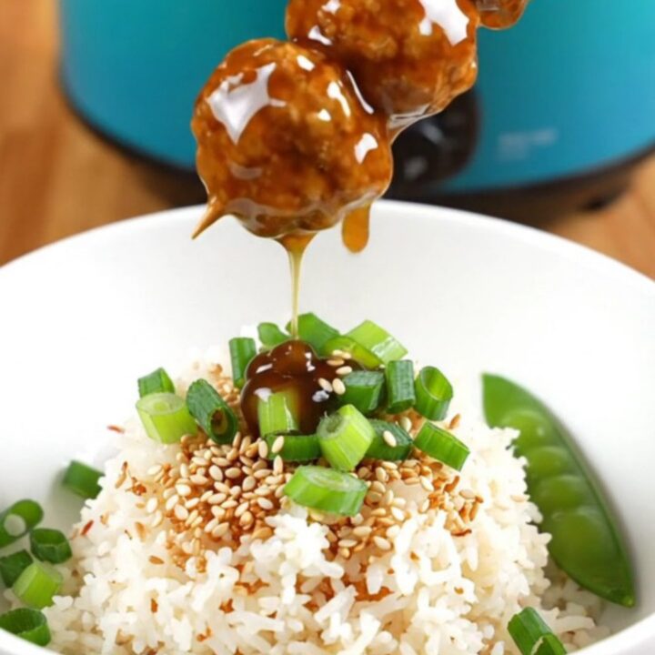 A close-up view of sticky teriyaki chicken meatballs glistening with glaze in a ceramic slow cooker.