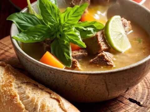 A steaming bowl of Vietnamese Bo Kho beef stew garnished with fresh herbs and lime.