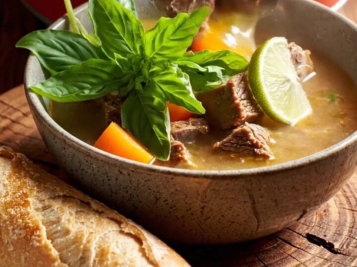 A steaming bowl of Vietnamese Bo Kho beef stew garnished with fresh herbs and lime.