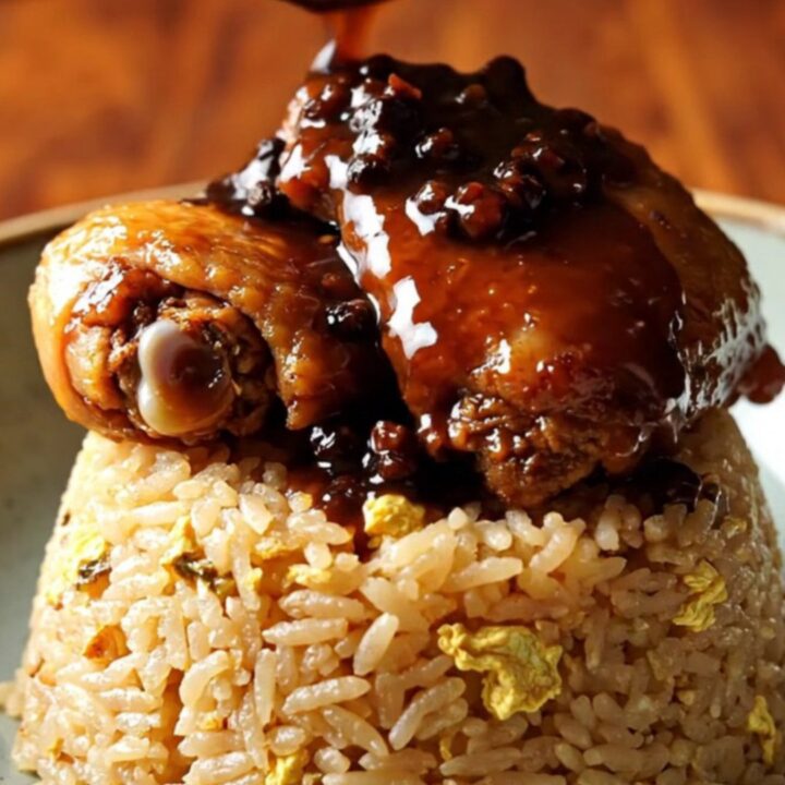 A close-up of tender chicken and pork belly adobo served over garlic fried rice in a bowl.