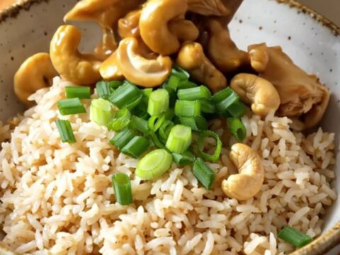 A ceramic slow cooker filled with cashew chicken, mushrooms, and baby corn in a rich, glossy brown sauce.