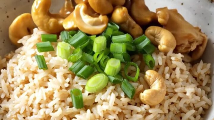 A ceramic slow cooker filled with cashew chicken, mushrooms, and baby corn in a rich, glossy brown sauce.