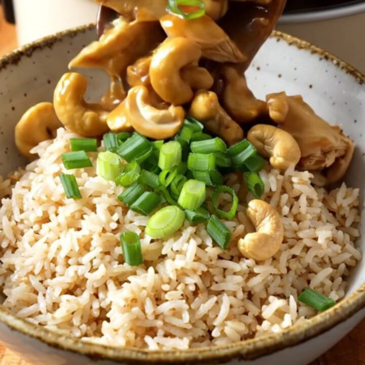 A ceramic slow cooker filled with cashew chicken, mushrooms, and baby corn in a rich, glossy brown sauce.