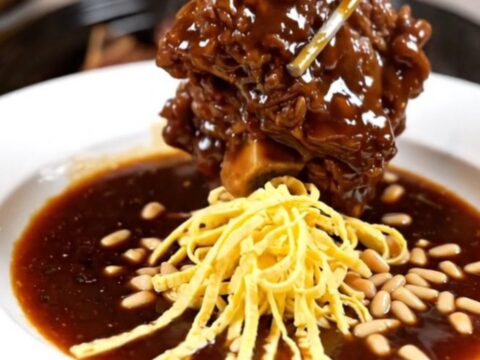 A cinematic close-up of tender Korean Galbi-Jjim braised short ribs in a glossy soy-pear glaze inside a ceramic slow cooker.