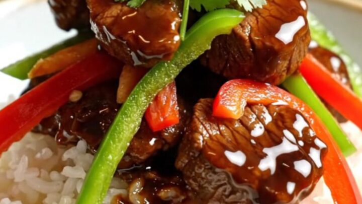 A close-up of tender sirloin steak strips and colorful bell peppers in a glossy black pepper sauce inside a ceramic slow