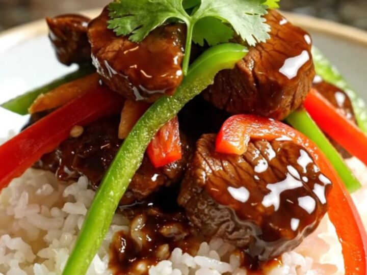 A close-up of tender sirloin steak strips and colorful bell peppers in a glossy black pepper sauce inside a ceramic slow