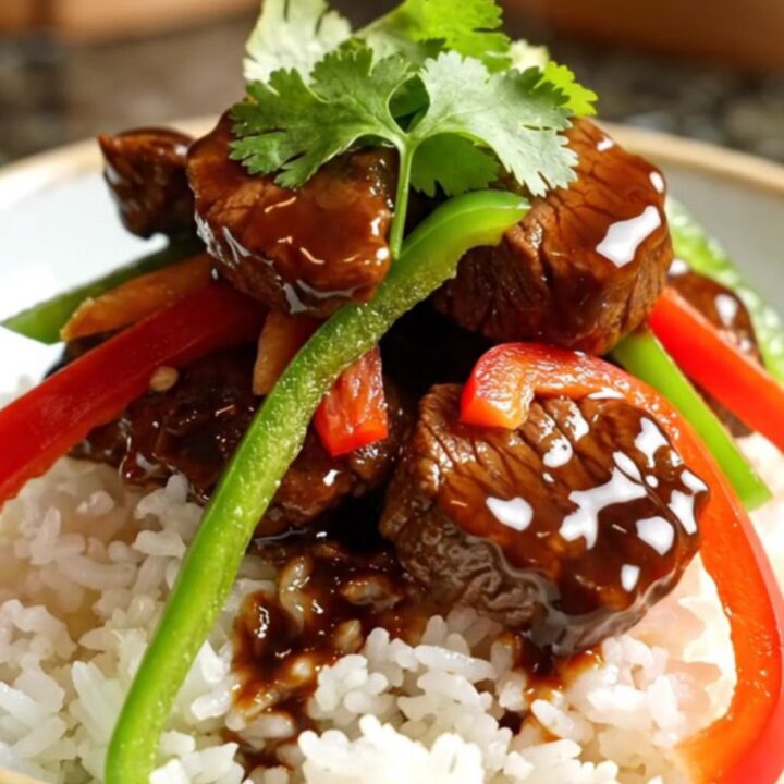 A close-up of tender sirloin steak strips and colorful bell peppers in a glossy black pepper sauce inside a ceramic slow