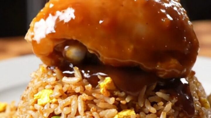 Sticky bourbon chicken thighs with a glossy glaze served over a bowl of fried rice.