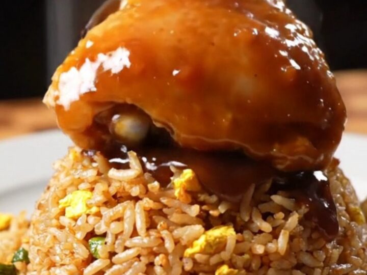 Sticky bourbon chicken thighs with a glossy glaze served over a bowl of fried rice.