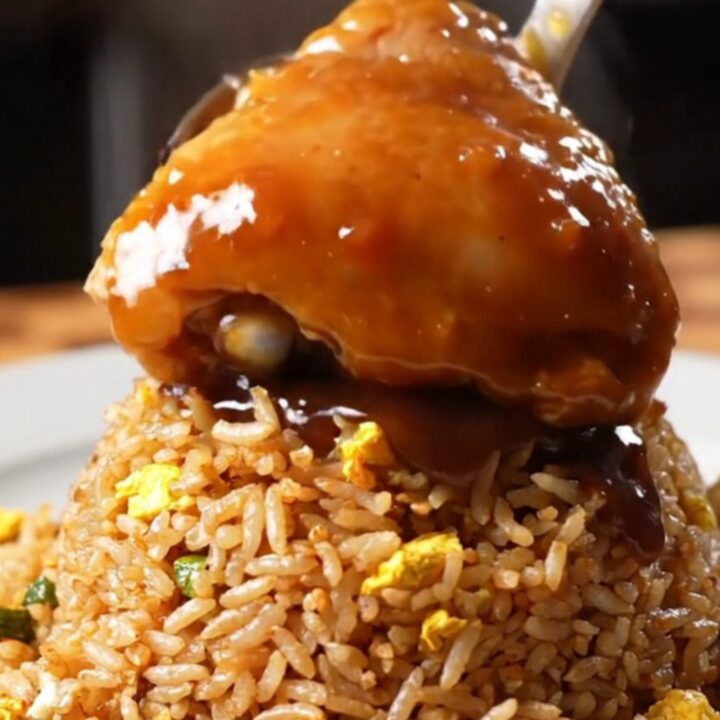 Sticky bourbon chicken thighs with a glossy glaze served over a bowl of fried rice.