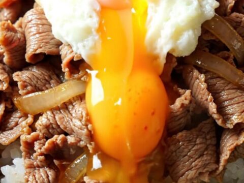A steaming bowl of Japanese Gyudon with tender beef and onions over rice, topped with a runny onsen egg.