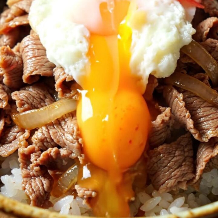 A steaming bowl of Japanese Gyudon with tender beef and onions over rice, topped with a runny onsen egg.