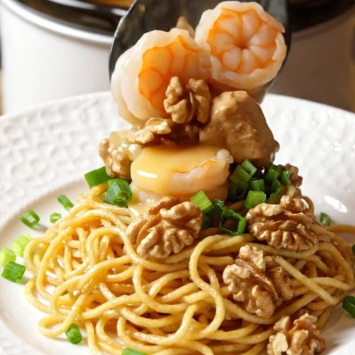 A close-up of honey walnut chicken and shrimp in a slow cooker with a creamy glaze and walnuts.