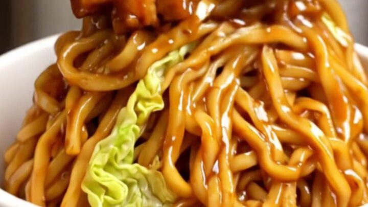 A close-up of glossy Char Siu pork lo mein noodles in a takeout bowl with mushrooms and carrots.