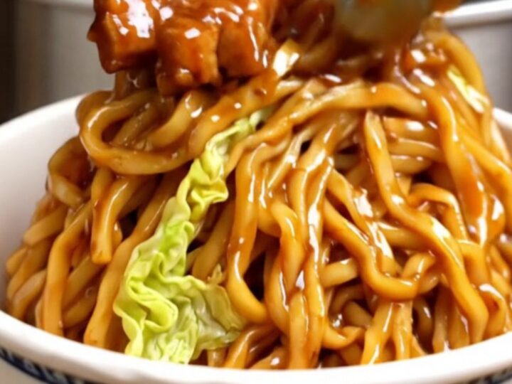 A close-up of glossy Char Siu pork lo mein noodles in a takeout bowl with mushrooms and carrots.