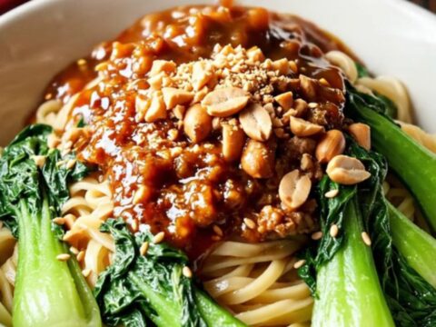 A close-up of a crimson-colored pork ragu served in a ceramic bowl with noodles.
