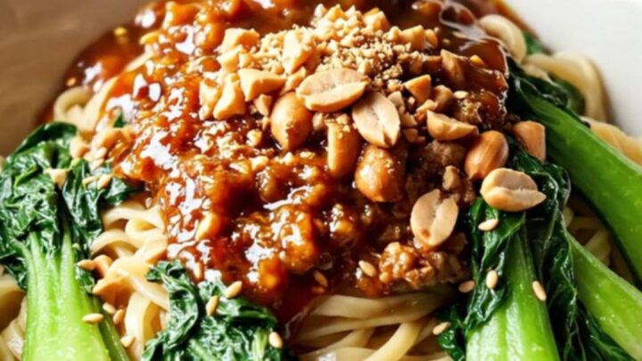A close-up of a crimson-colored pork ragu served in a ceramic bowl with noodles.