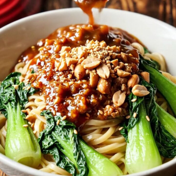 A close-up of a crimson-colored pork ragu served in a ceramic bowl with noodles.