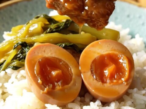 A ceramic slow cooker filled with braised pork belly cubes and dark mahogany eggs in a rich coconut caramel sauce.