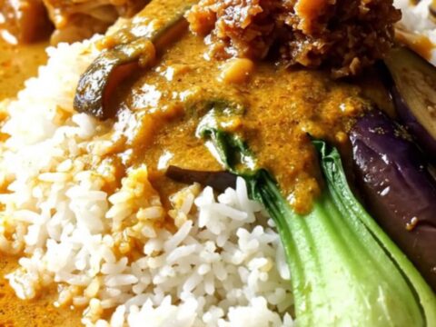 Close-up of golden-orange Filipino Kare-Kare with oxtails and vegetables in a ceramic Crockpot.